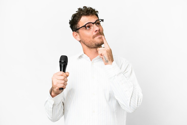 Homem brasileiro pegando um microfone sobre fundo branco isolado tendo dúvidas enquanto olha para cima