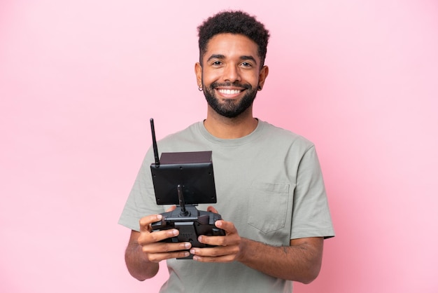 Foto homem brasileiro segurando um controle remoto de drone isolado em fundo rosa com expressão feliz