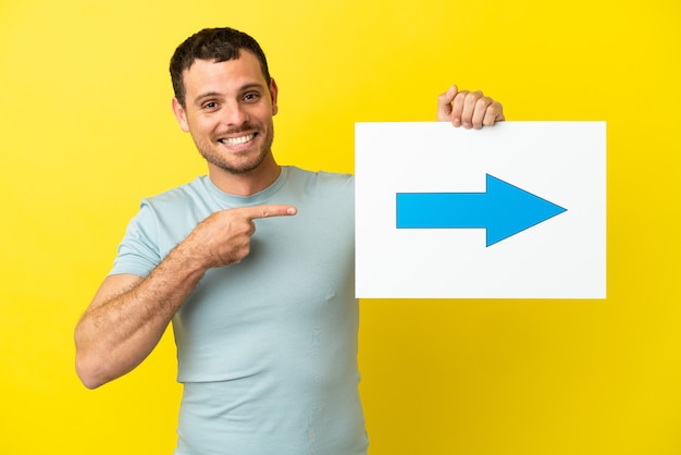 Homem brasileiro sobre fundo roxo isolado segurando um cartaz com o símbolo da seta e apontando-o