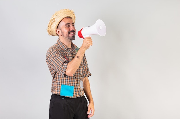 Homem brasileiro vestindo roupas de festa junina Arraial Festa de São João gritando promoção com megafone