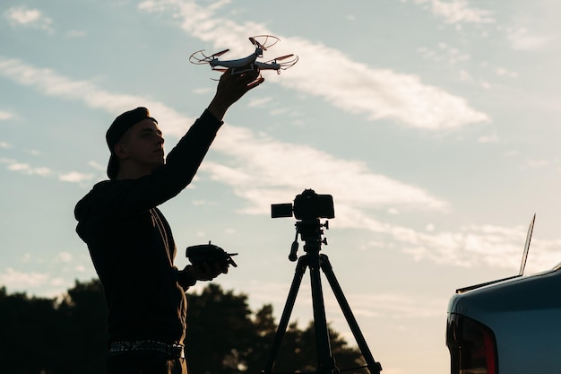 Homem brincando com silhueta de drone contra o céu do pôr do sol Jovem fotógrafo irreconhecível executando quadrocopter ao ar livre à noite Conceito de inovação de tecnologia de passatempo de lazer