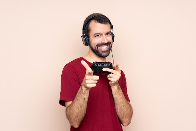 Homem brincando com um controlador de videogame sobre parede isolada, apontando para a frente e sorrindo