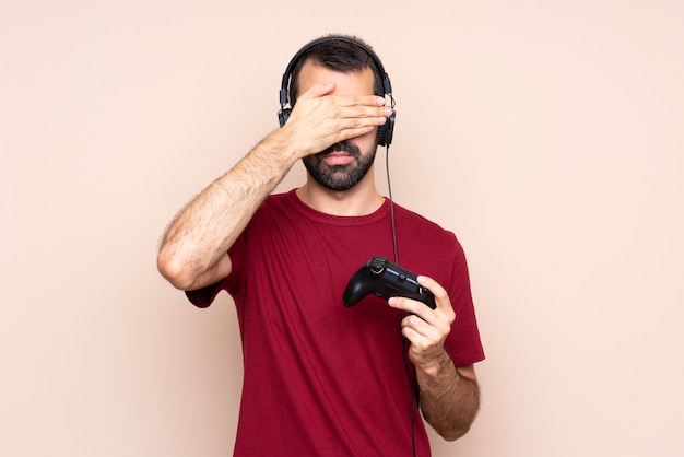 Homem brincando com um controlador de videogame sobre parede isolada, cobrindo os olhos pelas mãos. não quero ver algo