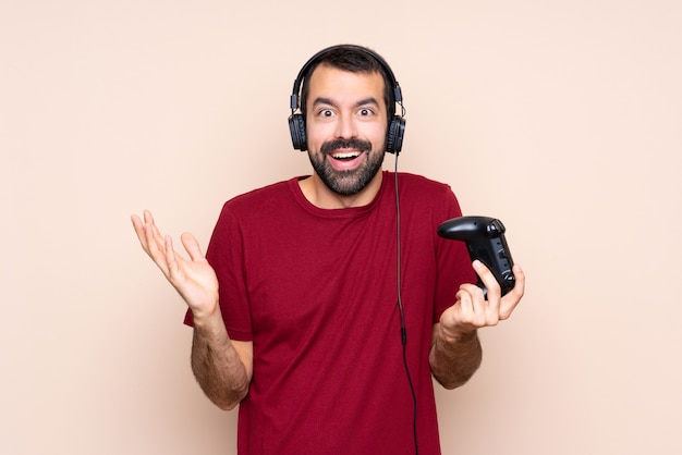 Homem brincando com um controlador de videogame sobre parede isolada com expressão facial chocada