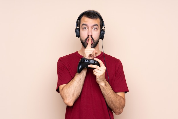 Homem brincando com um controlador de videogame sobre parede isolada, mostrando um sinal de gesto de silêncio colocando o dedo na boca