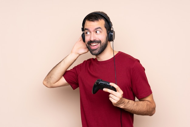 Homem brincando com um controlador de videogame sobre parede isolada, ouvindo algo, colocando a mão na orelha