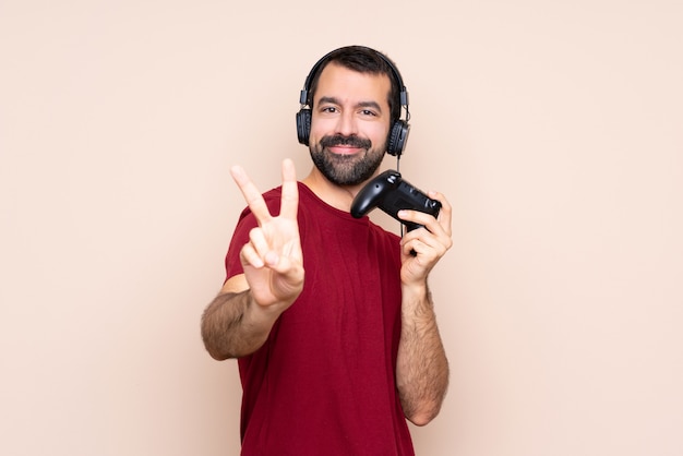 Homem brincando com um controlador de videogame sobre parede isolada sorrindo e mostrando sinal de vitória