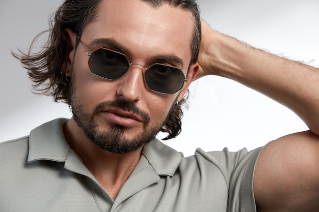 Homem brutal em óculos de sol, close-up, morena com barba por fazer em óculos elegantes em um fundo cinza.