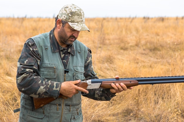 Homem caçador camuflado com uma arma durante a caça em busca de aves selvagens ou caça