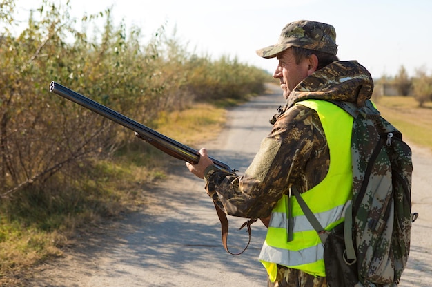 Homem caçador camuflado com uma arma durante a caça em busca de pássaros selvagens ou de caça
