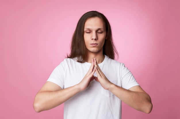 Homem calmo de mãos dadas em gesto de ioga, relaxando, meditando, tentando se acalmar em um fundo rosa