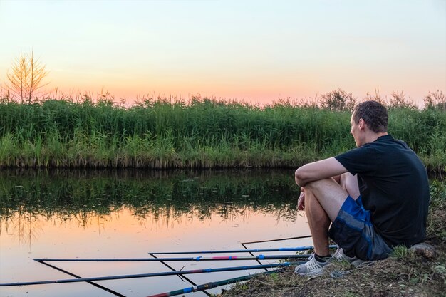 Homem calmo e relaxado pesca muito enquanto está sentado na margem do lago ao pôr do sol