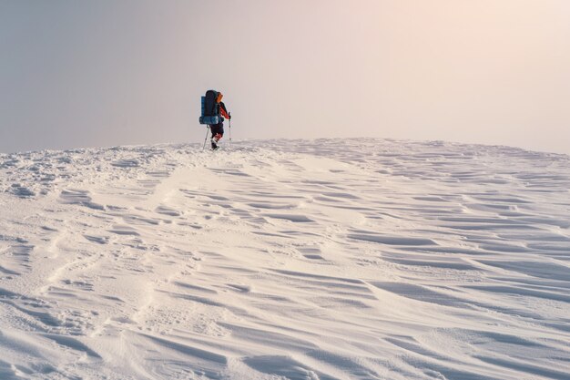 Homem, caminhadas com mochila e raquetes de neve na montanha do inverno