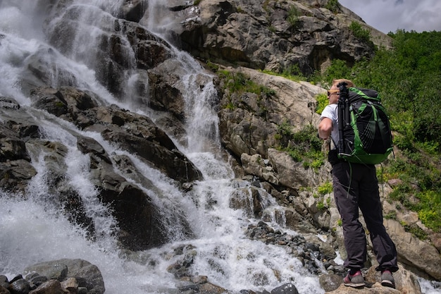 Homem caminhando com mochila olhando para a cachoeira Retrato de costas adultas masculinas em pé ao ar livre