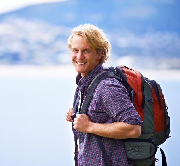 Foto homem caminhando e retrato em montanhas para viagem aventura e bem-estar pelo mar oceânico e férias na europa rosto de um jovem entusiasmado com mochila para caminhadas explorar e viagem ao ar livre