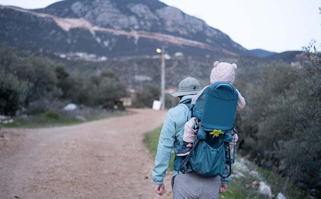 Homem caminhando nas montanhas carregando o bebê na mochilaslinguartransportadoraviagens em famíliaviagensestilo de vidapaifilho