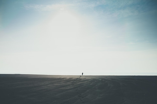 Foto homem caminhando sozinho ao horizonte na praia negra na islândia deixando pegadas