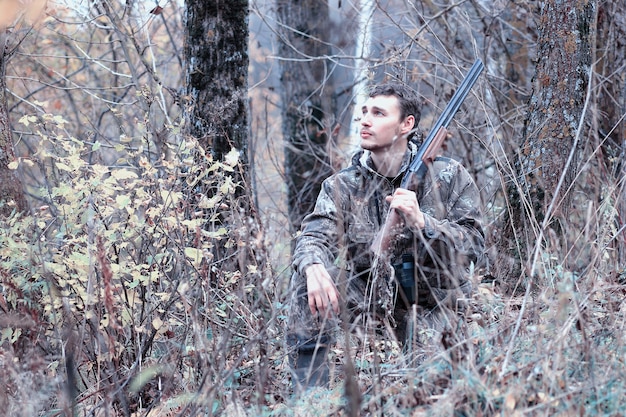 Homem camuflado e com um rifle de caça em uma floresta em uma caçada na primavera