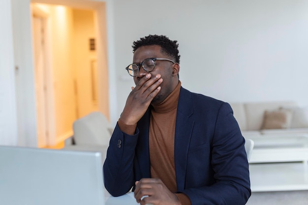 Homem cansado bocejando após um longo dia de trabalho Trabalho de manhã cedo Freelancer cansado com sono está bocejando em sua casa na frente da tela de laptops na mesa