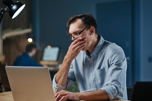 Homem cansado com laptop trabalhando no escritório noturno