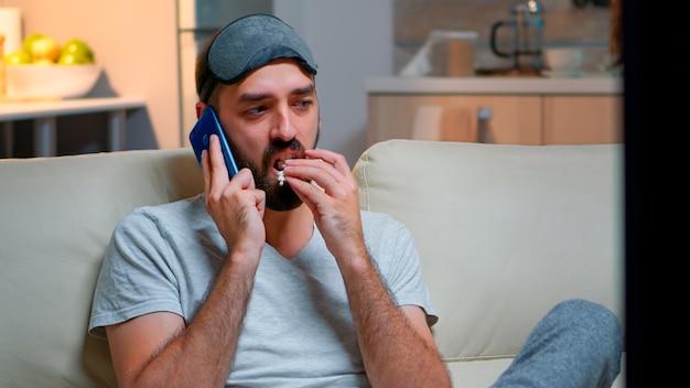 Homem cansado com máscara de dormir colocado falando no smartphone
