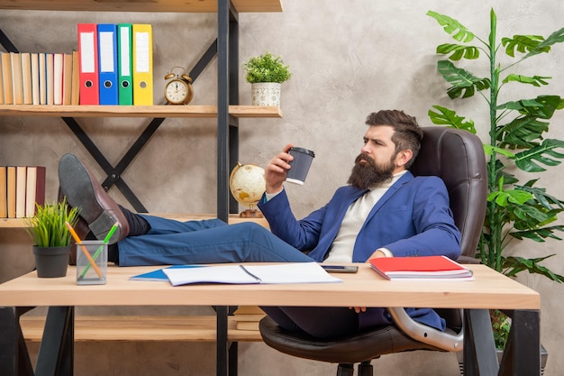 Homem cansado de terno relaxando com as pernas na mesa durante a pausa para o café no relaxamento do escritório