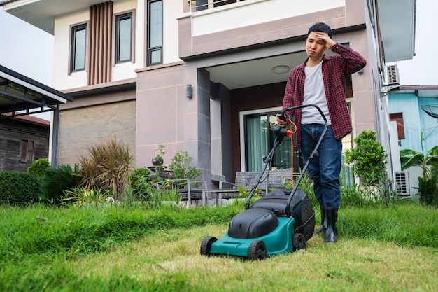 Homem cansado usando um cortador de grama cortando grama em casa