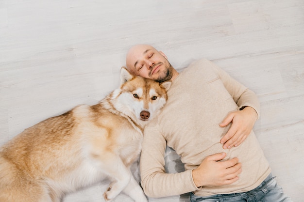 Homem careca adulto com filhote de cachorro husky dormindo no chão.