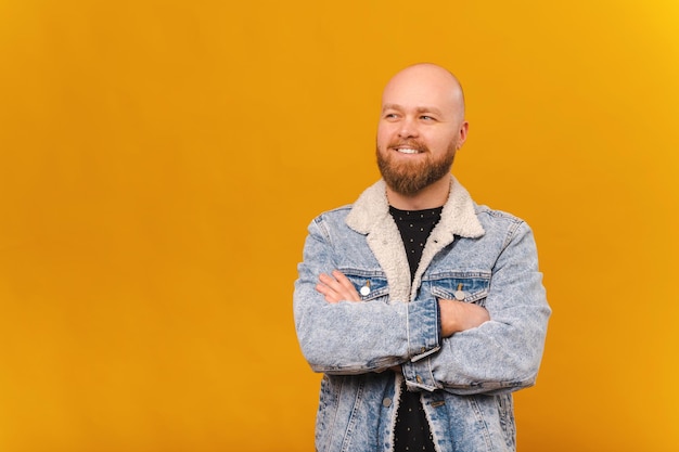 Homem careca barbudo sorridente confiante em jaqueta jeans está segurando os braços cruzados