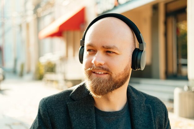 Homem careca bonito está ouvindo música ou podcast através de fones de ouvido