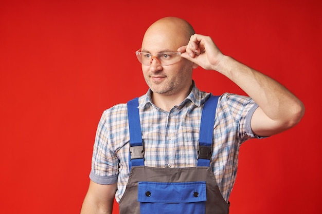 Homem careca em um terno de trabalho e óculos vermelhos aguarda com expectativa em um fundo vermelho