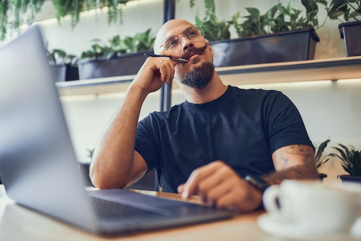 Foto homem careca escritor freelancer ou gerente sentado atrás de um laptop procurando ideias para um projeto