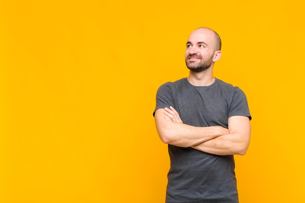 Homem careca se sentindo feliz, orgulhoso e esperançoso, imaginando ou pensando, olhando para cima para copiar o espaço com os braços cruzados