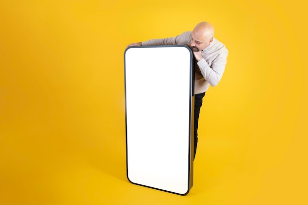 Homem careca segurando um telefone gigante com uma tela branca na frente dele