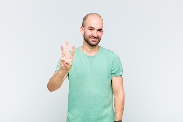 Homem careca sorrindo e parecendo amigável, mostrando o número três ou terceiro com a mão para a frente, em contagem regressiva