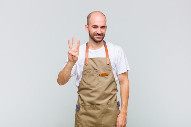 Homem careca sorrindo e parecendo amigável, mostrando o número três ou terceiro com a mão para a frente, em contagem regressiva