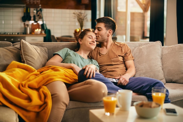 Homem carinhoso beijando sua namorada enquanto assiste TV em casa