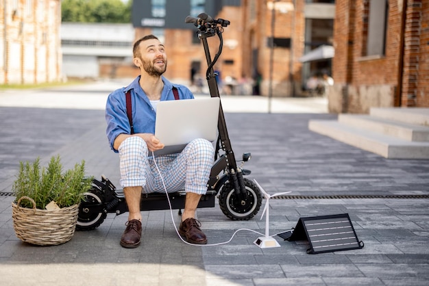 Homem carrega laptop com painéis solares enquanto está sentado na scooter elétrica ao ar livre