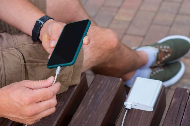 Homem carrega um smartphone com um banco de potência na mão Carregador portátil para carregar gadgets
