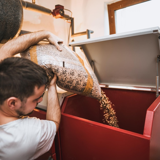 Homem carregando fogão de aquecimento a pellets Trabalhador em uma caldeira enchendo caldeira de pellets de madeira Sistema de aquecimento de biomassa