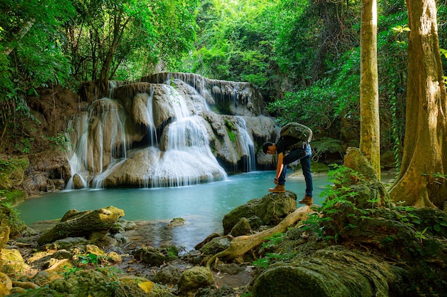 homem carregando uma mochila para viajar para a cachoeira, jovem com mochila em pé perto de uma cachoeira