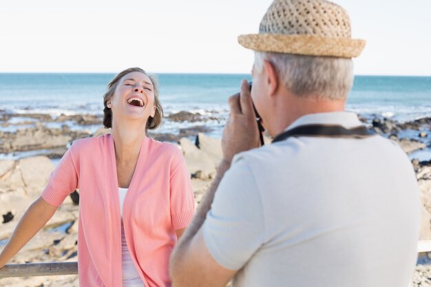 Homem casual feliz tomando uma foto de parceiro pelo mar