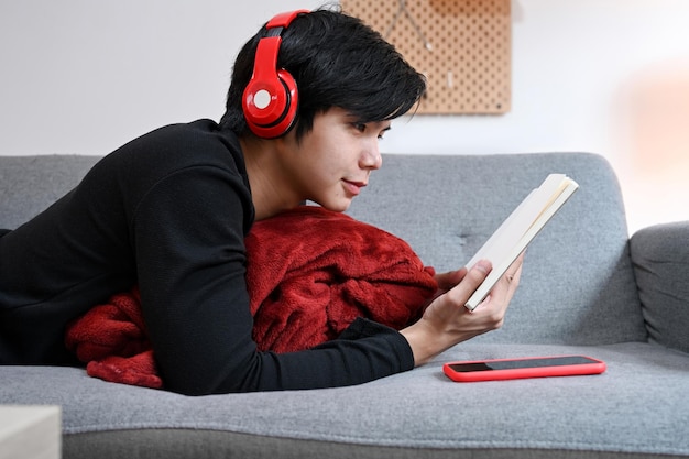 Homem casual ouvir música no fone de ouvido e ler livro no sofá