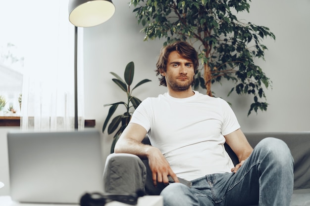 Homem casual relaxado sentado no sofá olhando para a câmera