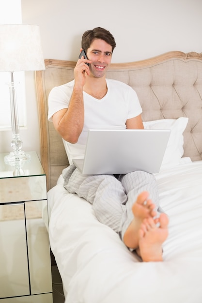 Homem casual usando celular e laptop na cama