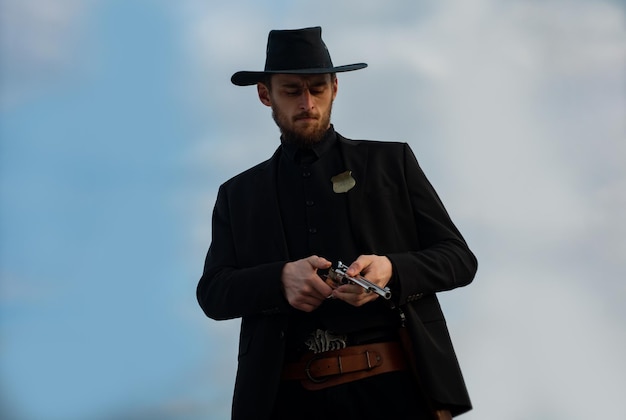 Homem caubói americano. Cara bonito e brutal do oeste. Xerife com armas do oeste selvagem, revólver de pistola vintage e munição de marechal. Western americano. Oeste selvagem com cowboy.