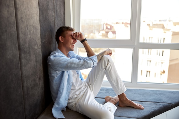 Homem caucasiano adulto feliz sentado perto de uma janela panorâmica e relaxando