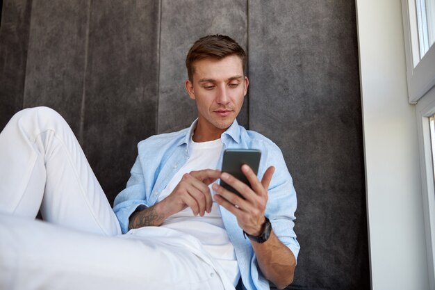 Homem caucasiano adulto feliz sentado perto de uma janela panorâmica e relaxando