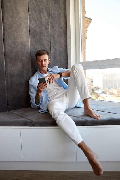 Homem caucasiano adulto feliz sentado perto de uma janela panorâmica e relaxando