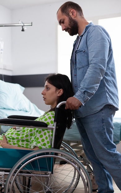 Homem caucasiano ajudando mulher grávida em cadeira de rodas